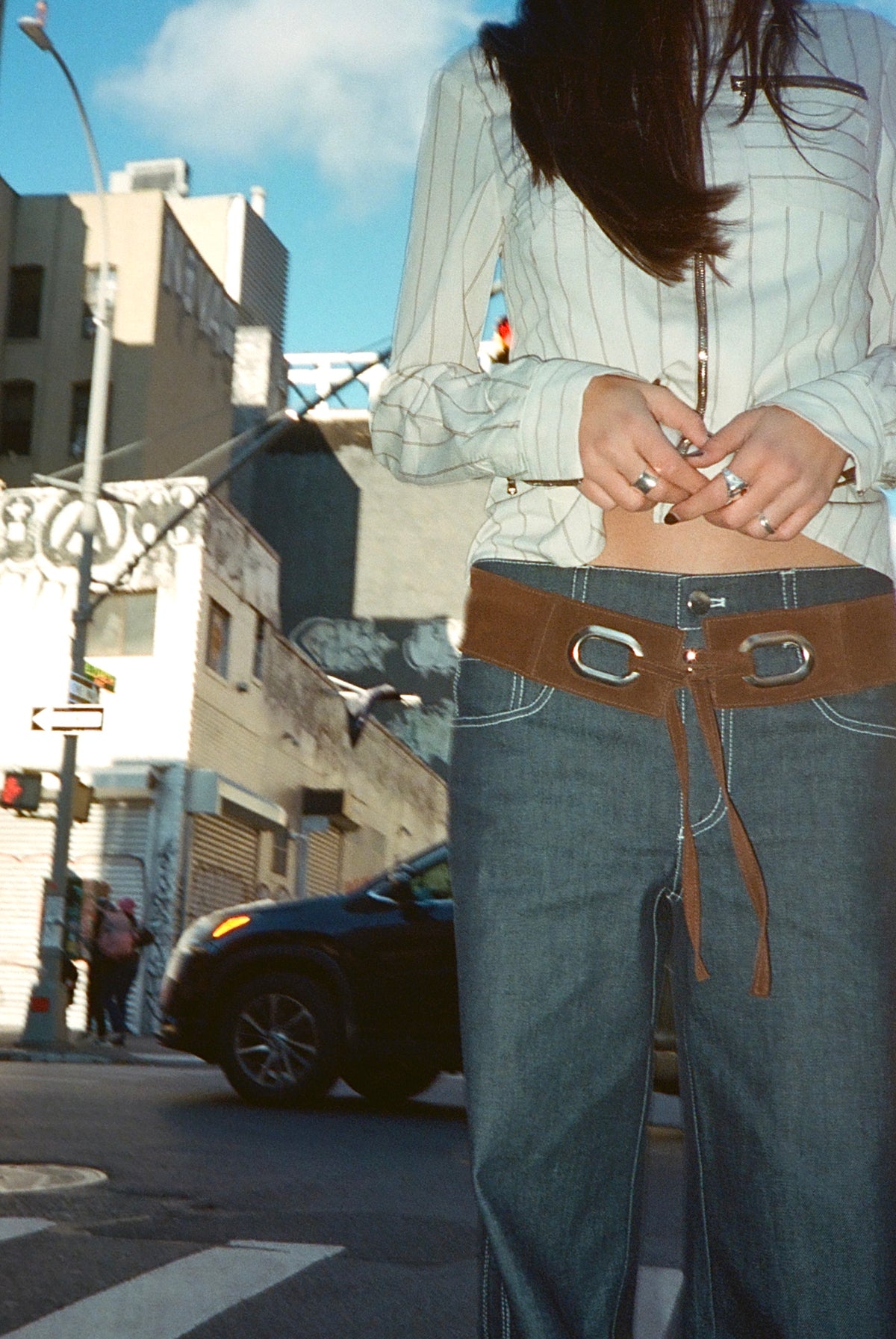 Close-up of the Beau Belt in Umber, a brown suede belt with silver eyelets and tie, worn low on dark jeans