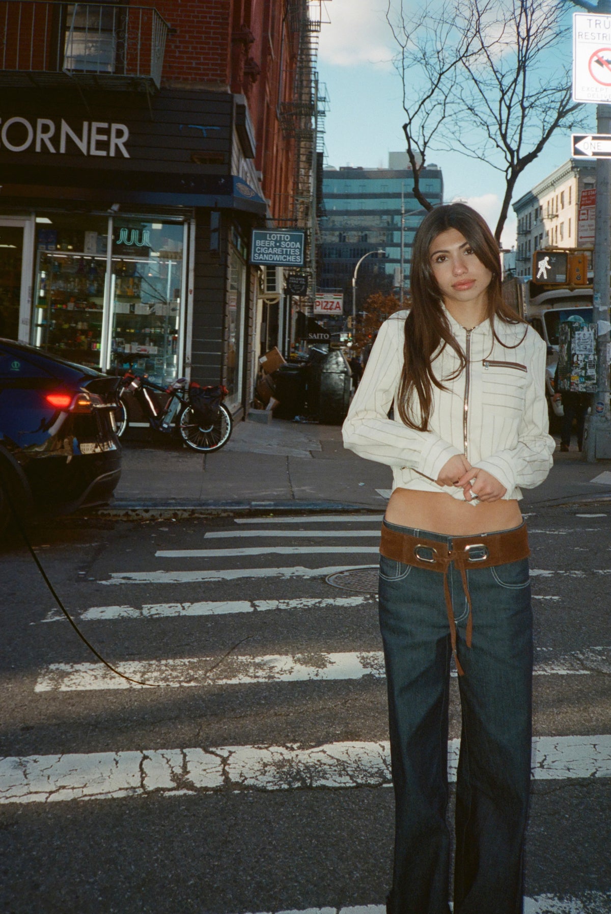 Model wearing the Beau Belt in Umber with dark jeans and a cream jacket at a crosswalk