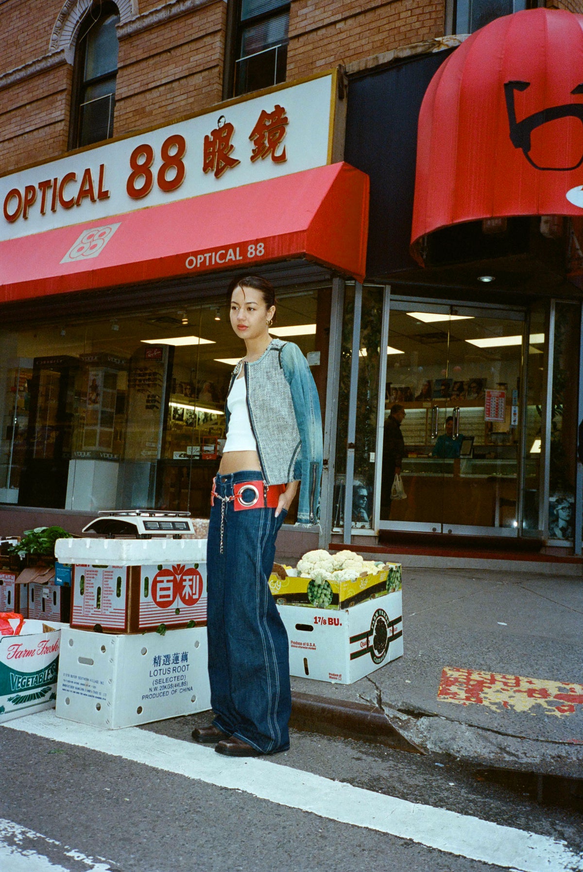 Model in the Lottie Jean in Indigo, a low-rise wide-leg raw denim jean, with a white tank outside an optical shop